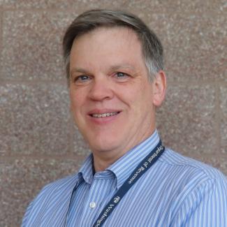 Headshot of Rob, a male-presenting person, with light skin tone, short grey hair, wearing a light blue button-down shirt.