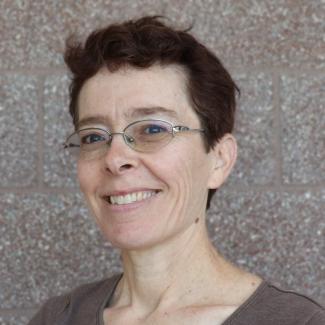 Headshot of Wendy, a person with light skin tone, short brown hair, wearing glasses and a brown shirt. 